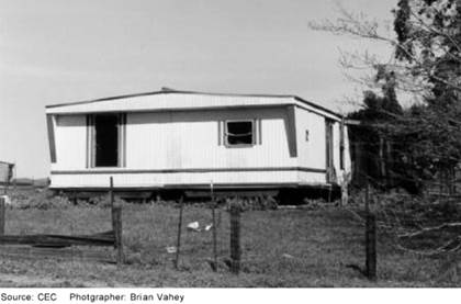 A manufactured or mobile home on a lot with grass and a fence